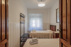 Una camera d'albergo con due letti, un armadio in legno, un comodino, un attaccapanni e una finestra con tende leggere.