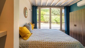Un dormitorio con cama, espejo y vista a la vegetación exterior.