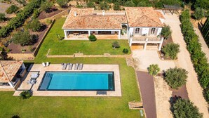 Vista aérea de una propiedad con piscina, un porche cubierto y una casa grande con techo de tejas.