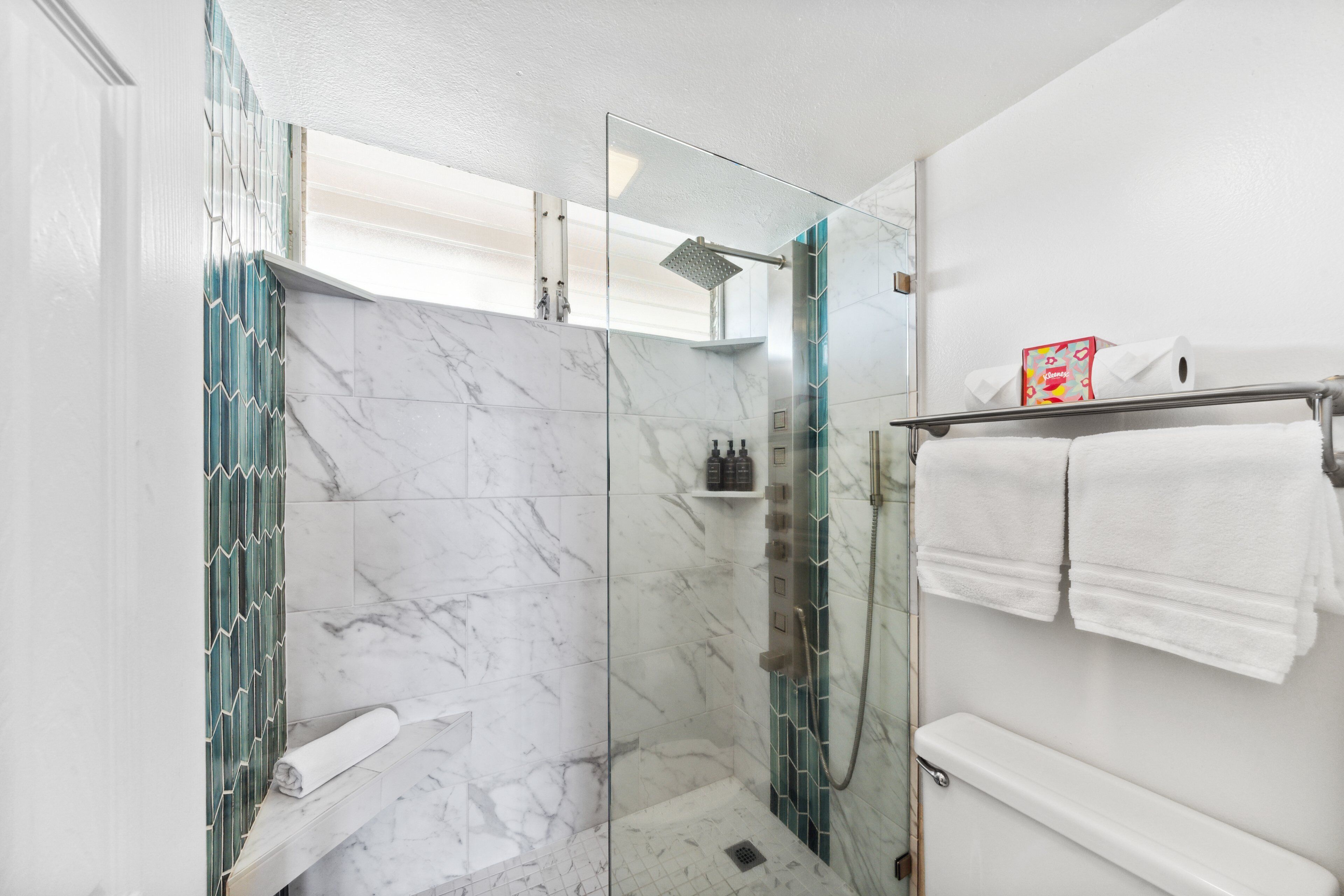 Un baño moderno con ducha de vidrio, azulejos de mármol, inodoro y toallero con toallas dobladas.