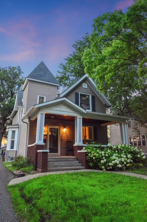 A two-story house with a steeply pitched roof, a front porch, and a well-maintained lawn. - Family Retreat: Sauna, Firepit & Downtown View (Saint Paul)