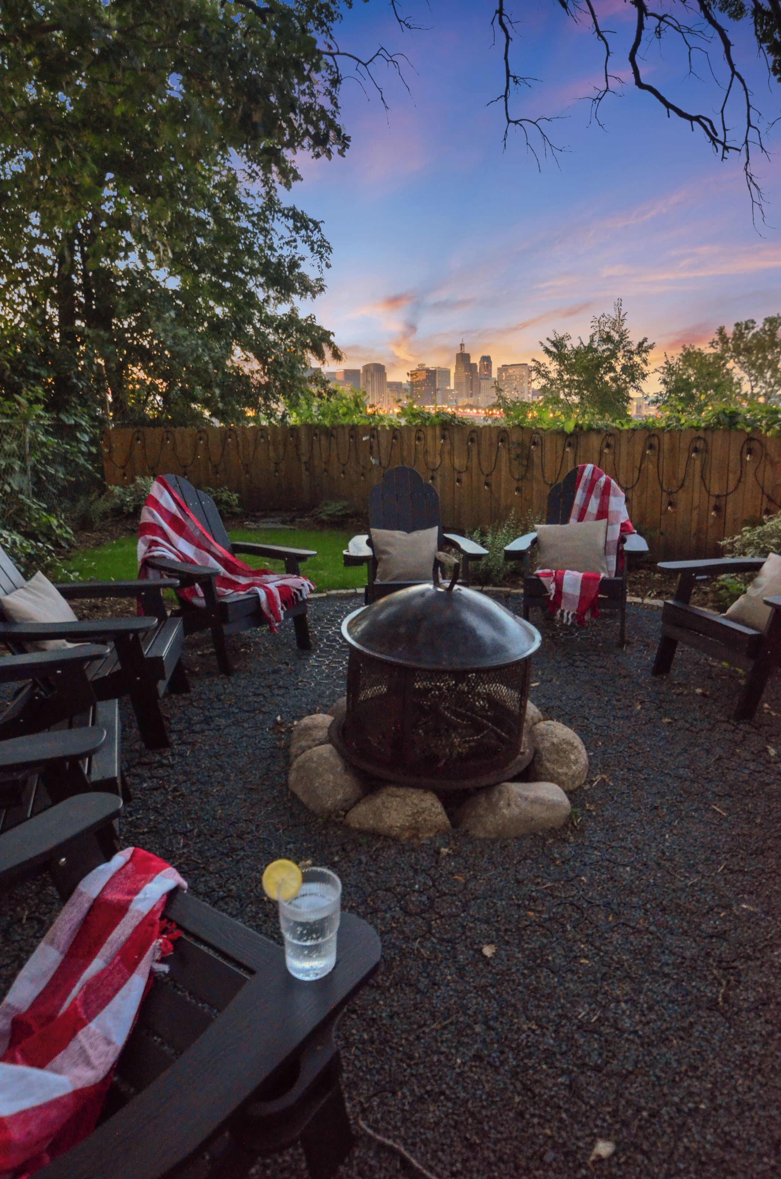 An outdoor seating area with chairs and a fire pit, a view of a city skyline in the background, and a wooden fence.