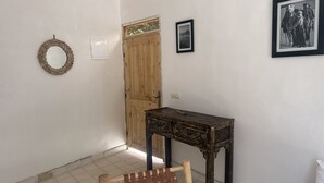 A room with a wooden door, a small table, a woven chair, and two framed pictures on the wall. - Chez Yahia, Au Coeur de l'Ourika, Studio le Nid des Aigles (Ourika)