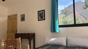 A room with a bed, a wooden chair, a small table, and a window with a view of a mountain. - Chez Yahia, Au Coeur de l'Ourika, Studio le Nid des Aigles (Ourika)