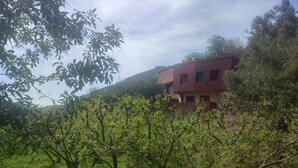 A rustic building with a sloped roof, surrounded by lush greenery and trees. - Chez Yahia, Au Coeur de l'Ourika, Studio le Nid des Aigles (Ourika)