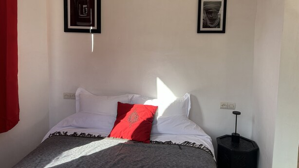 A bedroom with a bed, a red pillow, two framed pictures on the wall, and a bedside table with a lamp. - Chez Yahia, Au Coeur de l'Ourika, Studio le Nid des Aigles (Ourika)