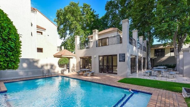 Une piscine à l’eau d’un bleu limpide, entourée d’une terrasse en briques et d’un bâtiment blanc doté d’un balcon.