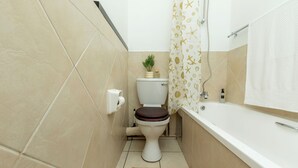 Une salle de bain avec des toilettes, une petite plante, un rideau de douche orné de motifs d’étoiles de mer et une baignoire.