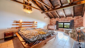 Een slaapkamer met een houten bed, een bakstenen muur, een uitzicht door een raam en een houten plafond.