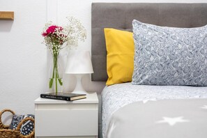 A neatly arranged bedroom with a grey upholstered headboard, a white bedside table, a lamp, a book, and a vase with flowers. - Vacation Apartment 'El Mirador' with Sea View, Shared Pool and Wi-Fi (Costa de Adeje)