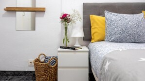 Un dormitorio ordenado con cama, mesita de noche, lámpara y estante en la pared.