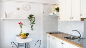 Una cocina con armarios blancos, encimera de madera, un fregadero, un reloj, un jarrón con flores y una planta colgante.