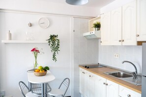 A kitchen with white cabinets, a wooden countertop, a sink, a clock, a vase with flowers, and a hanging plant. - Vacation Apartment 'El Mirador' with Sea View, Shared Pool and Wi-Fi (Costa de Adeje)