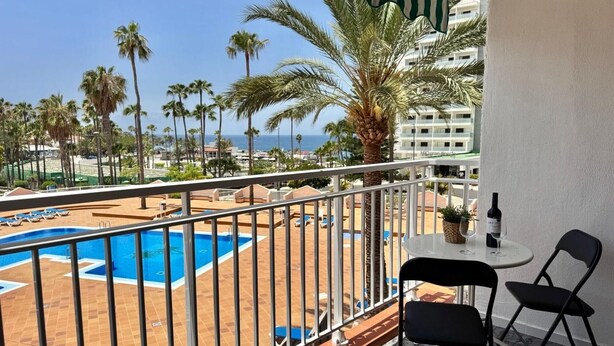Un balcón con piscina, sillas y una mesa con una botella y vasos.