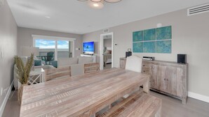 A spacious living area with a wooden dining table, a comfortable sofa, and a television. - Leonardo Arms 623 Beachfront 2B/2B Vacation Condo! Panoramic Gulf View! (Fort Myers Beach)