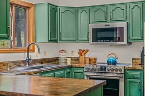 A kitchen with green cabinets, a stainless steel stove, and a microwave. - Skyefall Mountain Retreat: Hot Tub, Fire Pit & Wooded Views | Great for Families (Berkeley Springs)