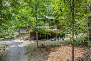 A two-story building with a covered patio area, surrounded by trees and a gravel driveway. - Skyefall Mountain Retreat: Hot Tub, Fire Pit & Wooded Views | Great for Families (Berkeley Springs)