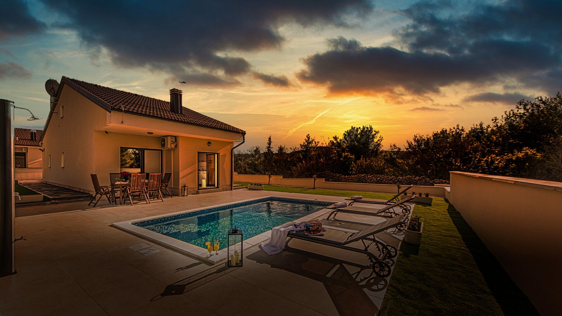 Una casa moderna con piscina, muebles de patio y vista al atardecer.