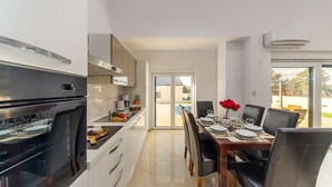 A modern kitchen with a built-in oven and a dining area with a table set for four. - Villa Shaula 2 by Villas Guide (Sibenik)