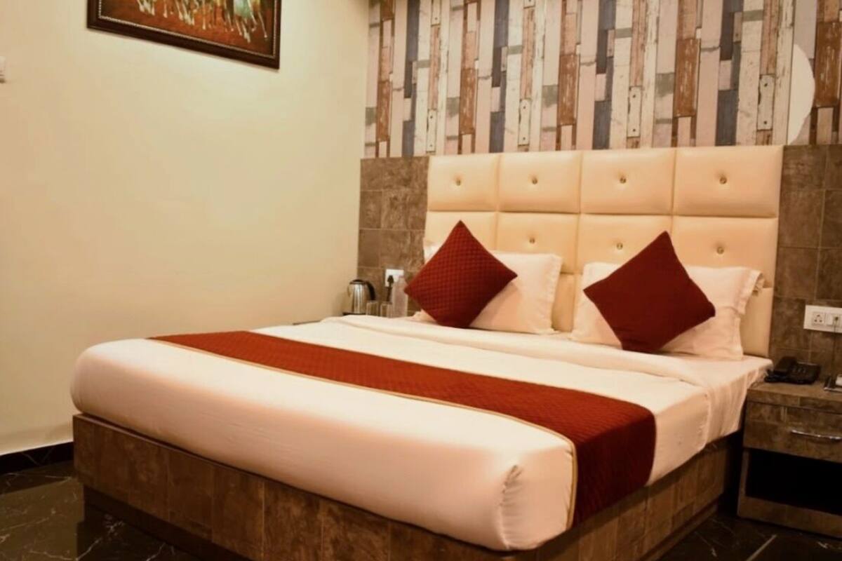Quarto de hotel com uma cama grande, cabeceira com botões, duas almofadas, mesa de cabeceira e um quadro na parede.