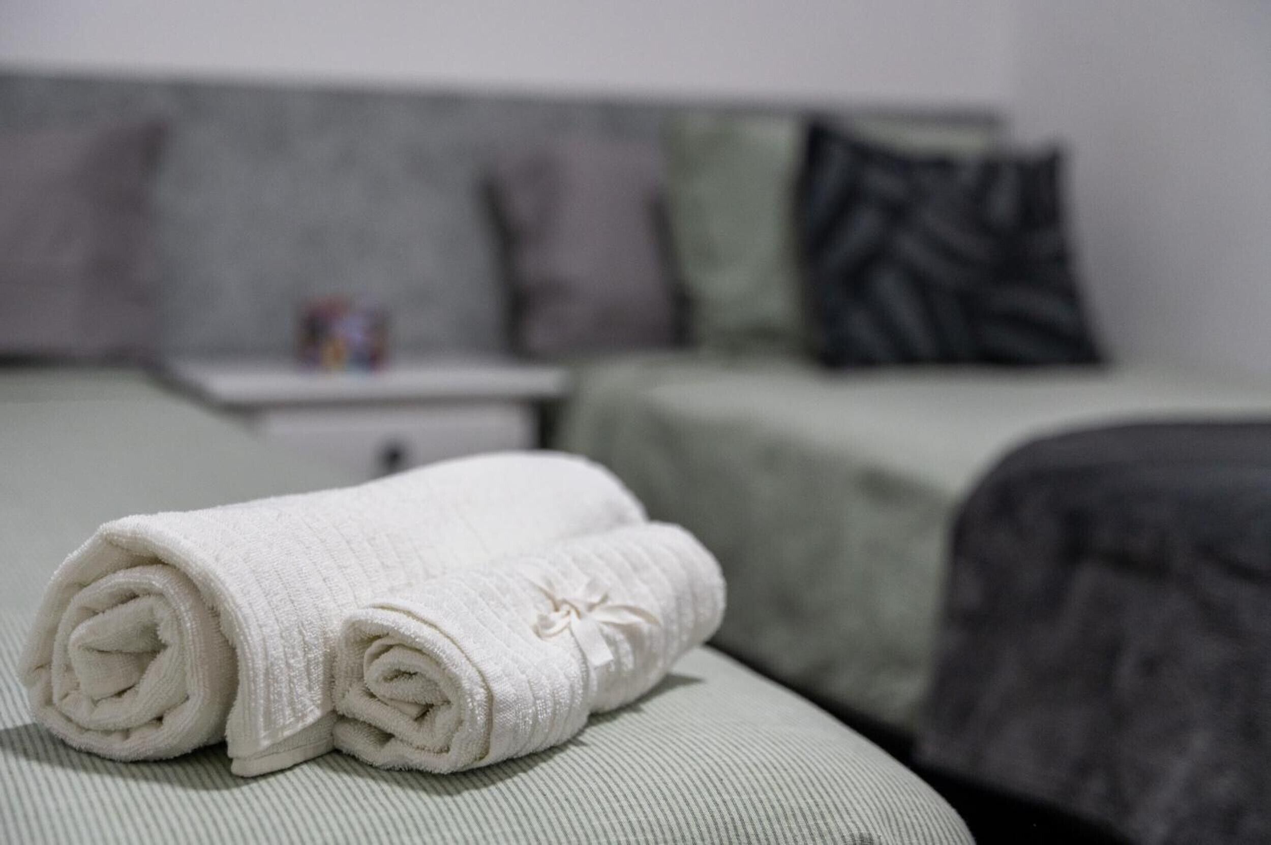 A neatly made white towel on a bed with a striped pillow and a gray headboard.