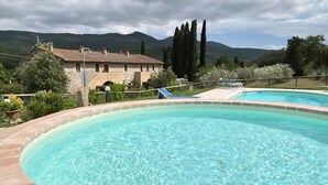 Ein Schwimmbecken mit Steinumrandung, ein Gebäude mit Flachdach und eine gebirgige Landschaft im Hintergrund.