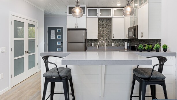 A modern kitchen with a large island, two bar stools, and pendant lighting.