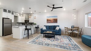 A modern kitchen with a built-in island, a dining area with a blue sofa and wooden table, and a ceiling fan.