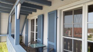 Un portico coperto con due tavoli e sedie, una finestra con persiane e vista su una zona residenziale.