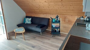 Un soggiorno moderno con un divano grigio, un piccolo tavolo di legno e un angolo cottura con lavello e piano di lavoro.