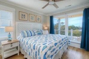A bedroom with a bed, nightstands, a ceiling fan, and a view of the outdoors. - Experience oceanfront luxury at Tortuga by the Sea in Oak Island, NC. (Oak Island)