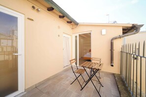 A small patio with a wooden table and chairs, a door leading to a bedroom, and a metal fence.