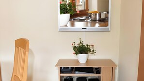 A room with a TV mounted on the wall, a wooden chair, a small table with a potted plant, and a speaker cabinet. - Holiday Apartment 'Scharbachhof' with Mountain View, Shared Garden and Wi-Fi (Glottertal)