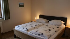 A double bed with a headboard, two bedside tables with lamps, a window with curtains, and a framed picture on the wall. - Holiday Apartment 'Scharbachhof' with Mountain View, Shared Garden and Wi-Fi (Glottertal)