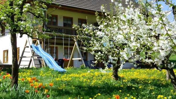 A residential area with a playground, a house with a sloped roof, and a garden with flowers. - Holiday Apartment 'Scharbachhof' with Mountain View, Shared Garden and Wi-Fi (Glottertal)