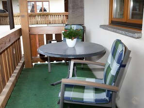 A round table with a potted plant, a plaid chair, and a wooden deck.