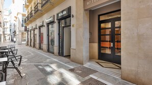 A street with outdoor seating, a building with a sign reading 'OFICEN TRO,' and a storefront with 'TUI & JON' and 'PERFUMERIA COSMETICA' signs. - ‘Málaga Centro Bonito’ Apartment with Balcony, Wi-Fi and Air Conditioning (Málaga)