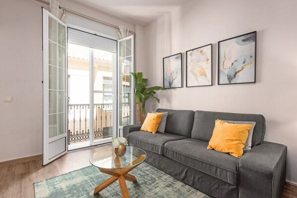 A living room with a grey sofa, a glass coffee table, and a large window with a balcony. - ‘Málaga Centro Bonito’ Apartment with Balcony, Wi-Fi and Air Conditioning (Málaga)