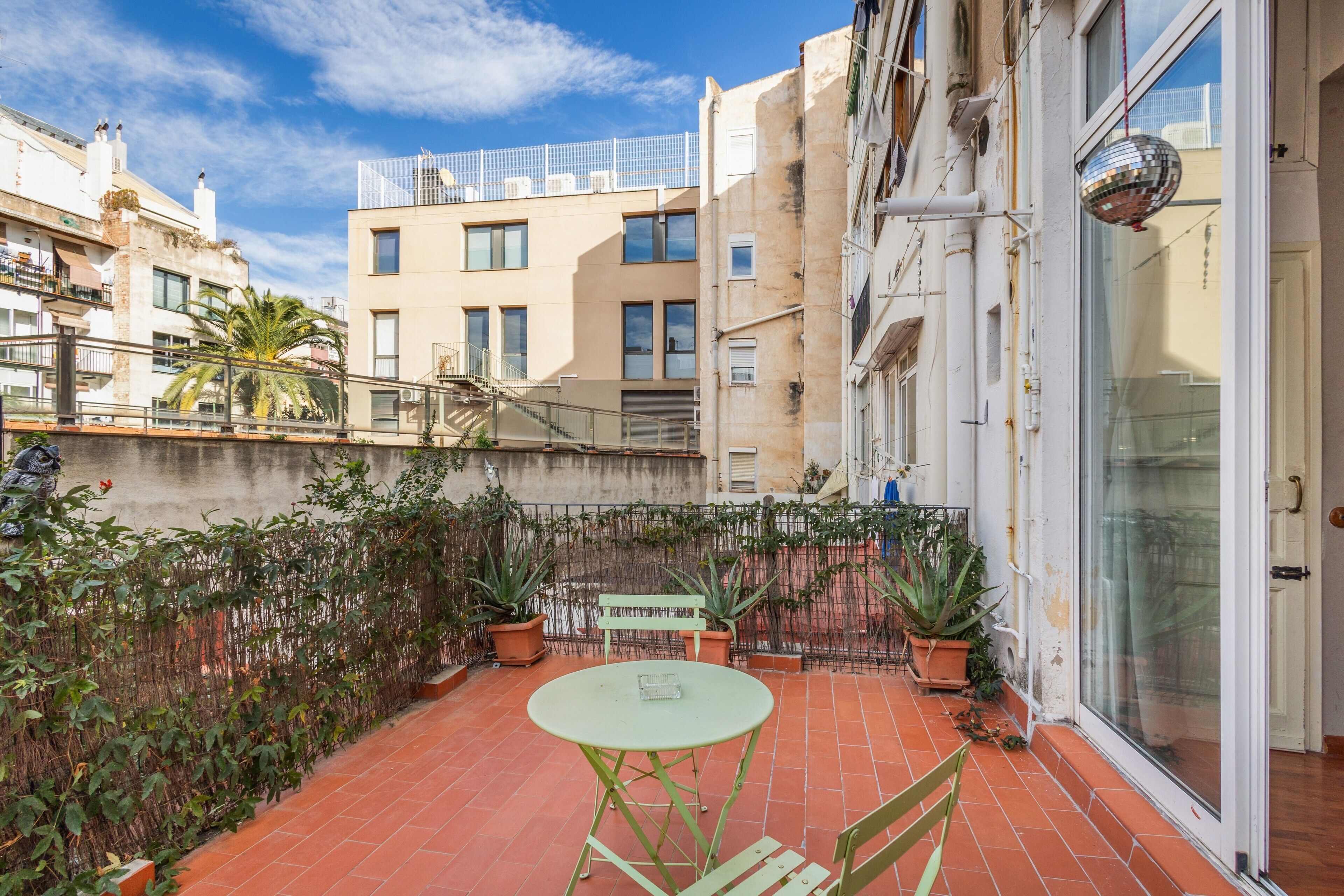Una terraza con mesa y sillas, plantas en macetas y vistas de edificios cercanos.