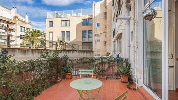 Una terraza con mesa y sillas, plantas en macetas y vistas de edificios cercanos.