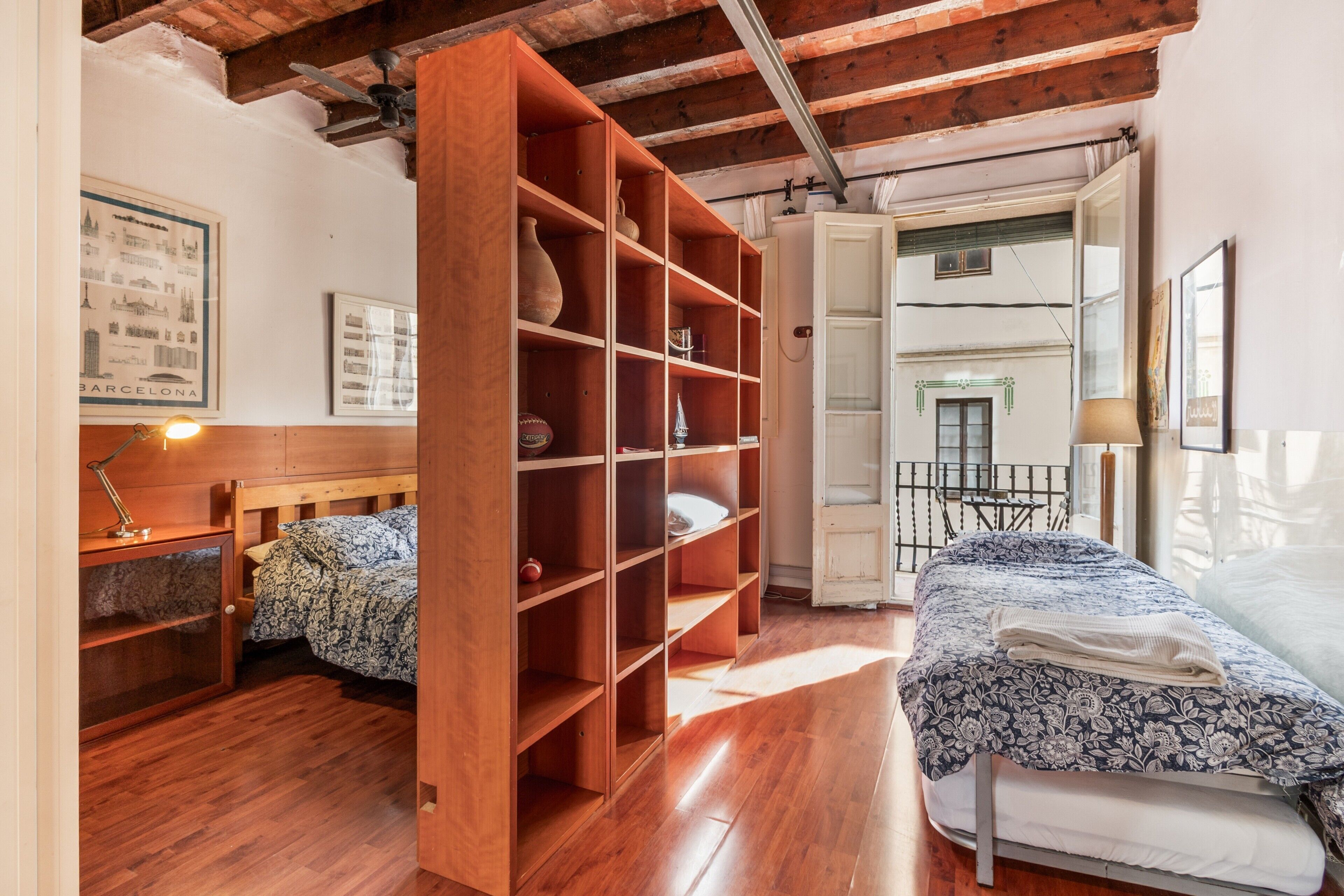 Una habitación con una cama de madera, un estante abierto grande, un escritorio con una lámpara y vistas al exterior.