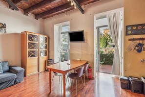 Una habitación con una mesa de comedor de madera, sillas, un sofá, un televisor montado en la pared y vistas a través de una puerta abierta.