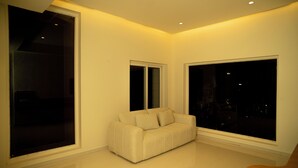 Una sala de estar moderna con un sofá, ventanas amplias y una lámpara empotrada en el techo.