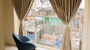 Una habitación con un ventanal grande, una silla azul y vista a una obra en construcción.