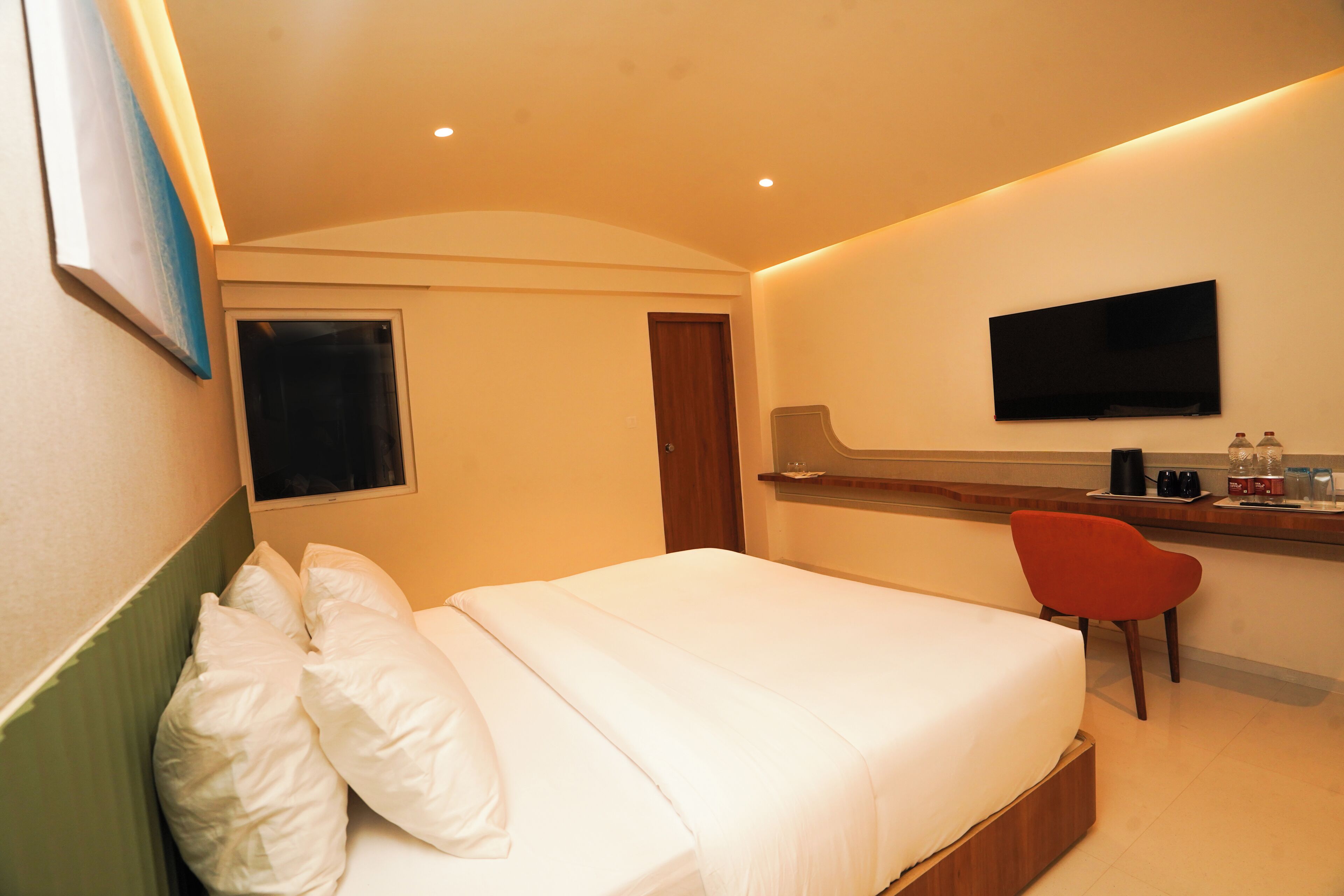 Une chambre d’hôtel avec un lit, un téléviseur fixé au mur, un bureau avec une chaise et une fenêtre.