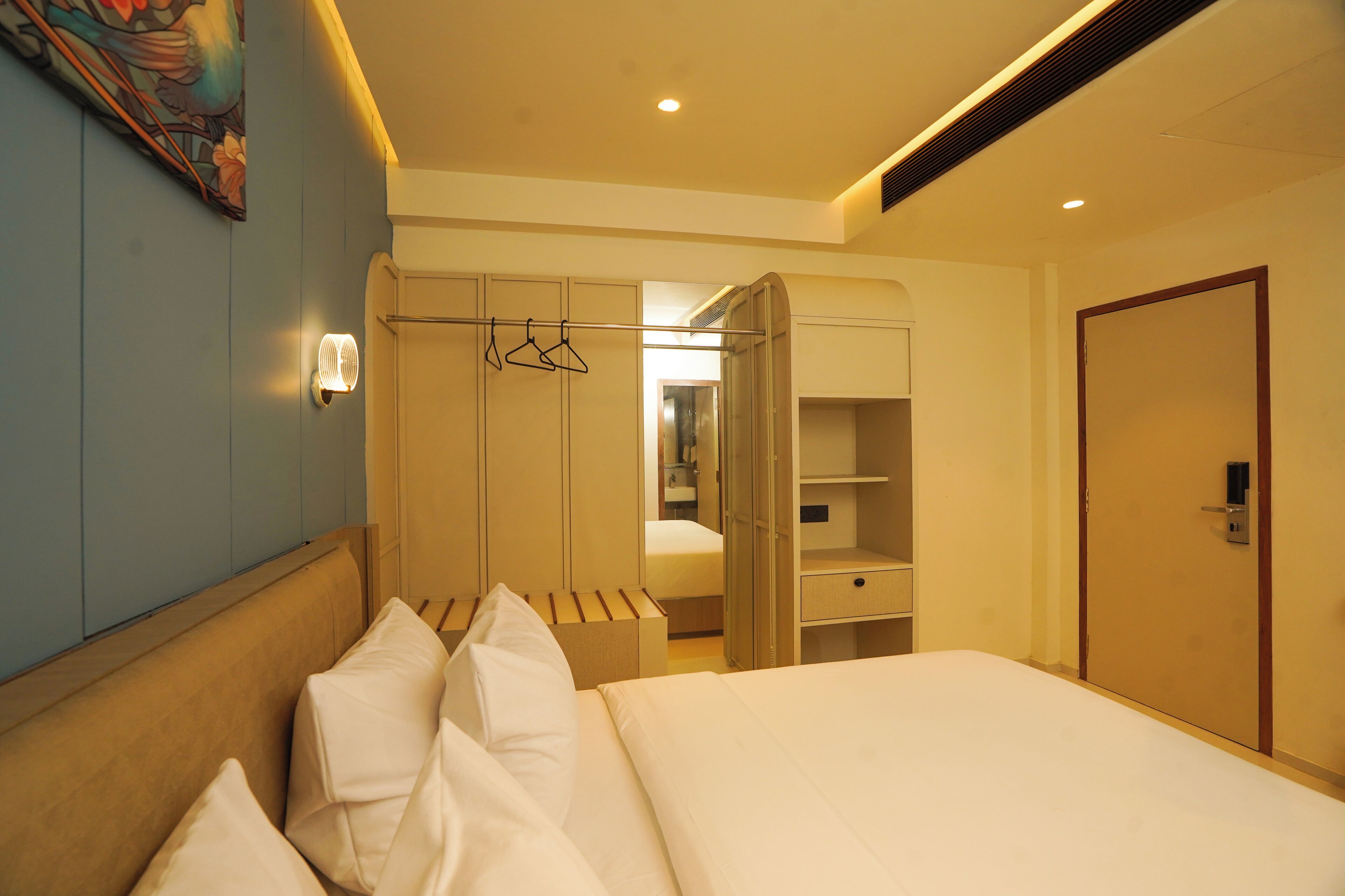 A hotel room with a bed, a wardrobe, a mirror, and a painting on the wall.