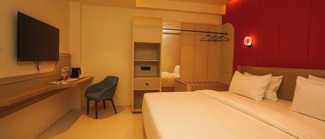 Habitación de hotel con cama, escritorio, silla, televisor y armario.