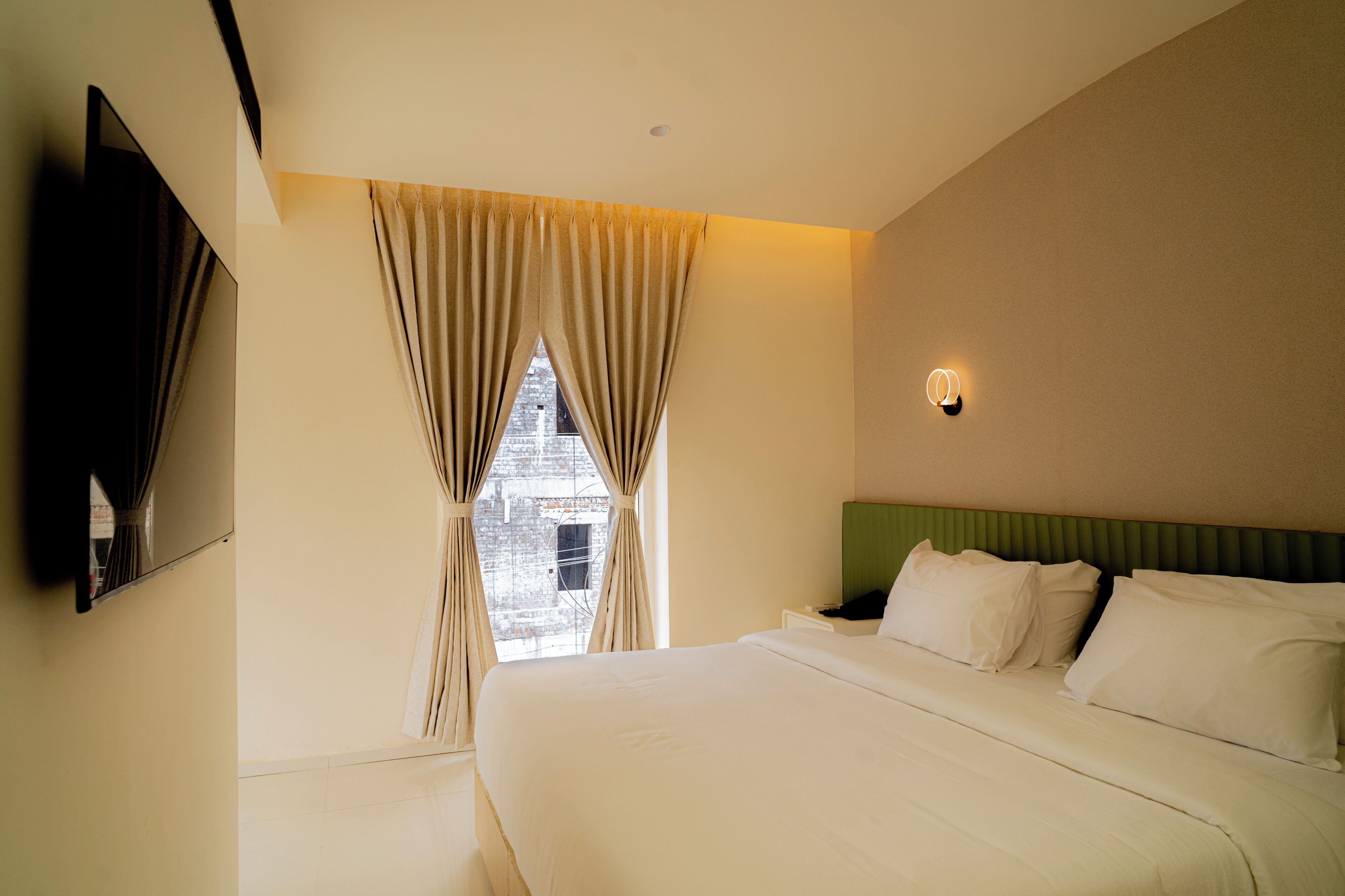 Habitación de hotel con una cama grande, un televisor de pantalla plana en la pared y una ventana con cortinas.