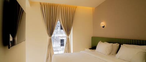 Habitación de hotel con una cama grande, un televisor de pantalla plana en la pared y una ventana con cortinas.