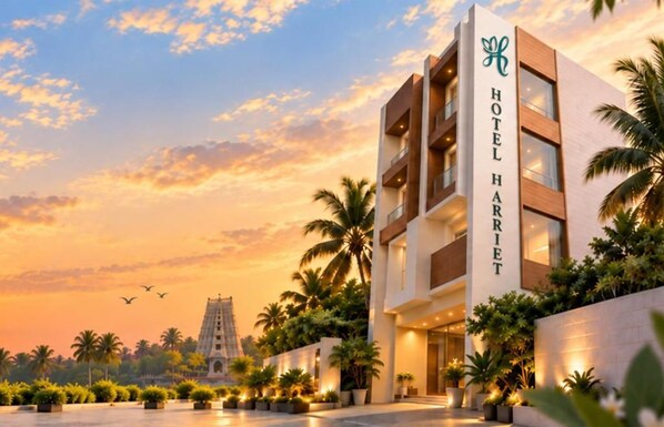 Un hotel moderno con un letrero llamativo, rodeado de palmeras y un cielo despejado.